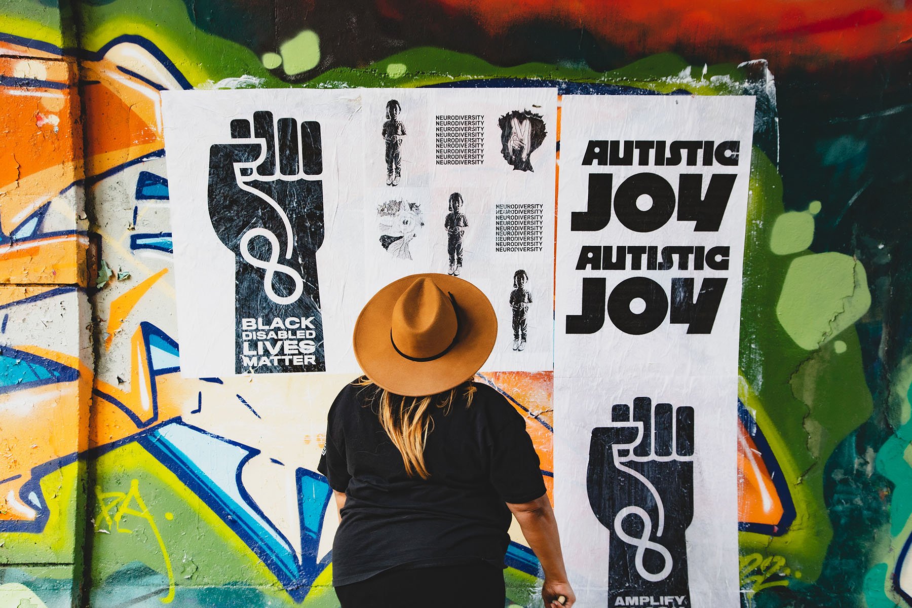 Jen White Johnson looks at wheat pastes she designed that read "autistic joy," "black disabled lives matter," and the word "neurodiversity" repeated throughout a poster.