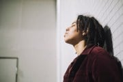 Non-binary person with eyes closed leaning on bathroom wall.