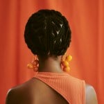 an unrecognized woman standing with braided hair with her back towards the camera.