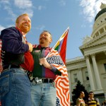 With an American flag draped over their shoulders and a rainbow flag in hand, Jim Gatteau and Mike Holland take part in a rally for gay marriage rights in front of the California state capitol.