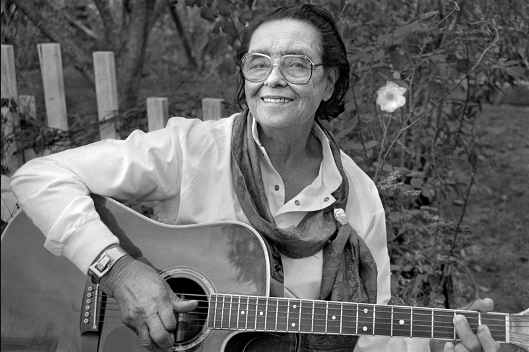 Country musician Etta Baker playing the guitar and smiling in a garden.