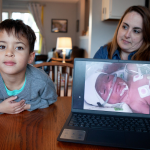 Emily Schmit and her son at their kitchen table. A photo of Emily's son as an infant in the NICU is displayed on a laptop near them.