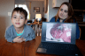 Emily Schmit and her son at their kitchen table. A photo of Emily's son as an infant in the NICU is displayed on a laptop near them.