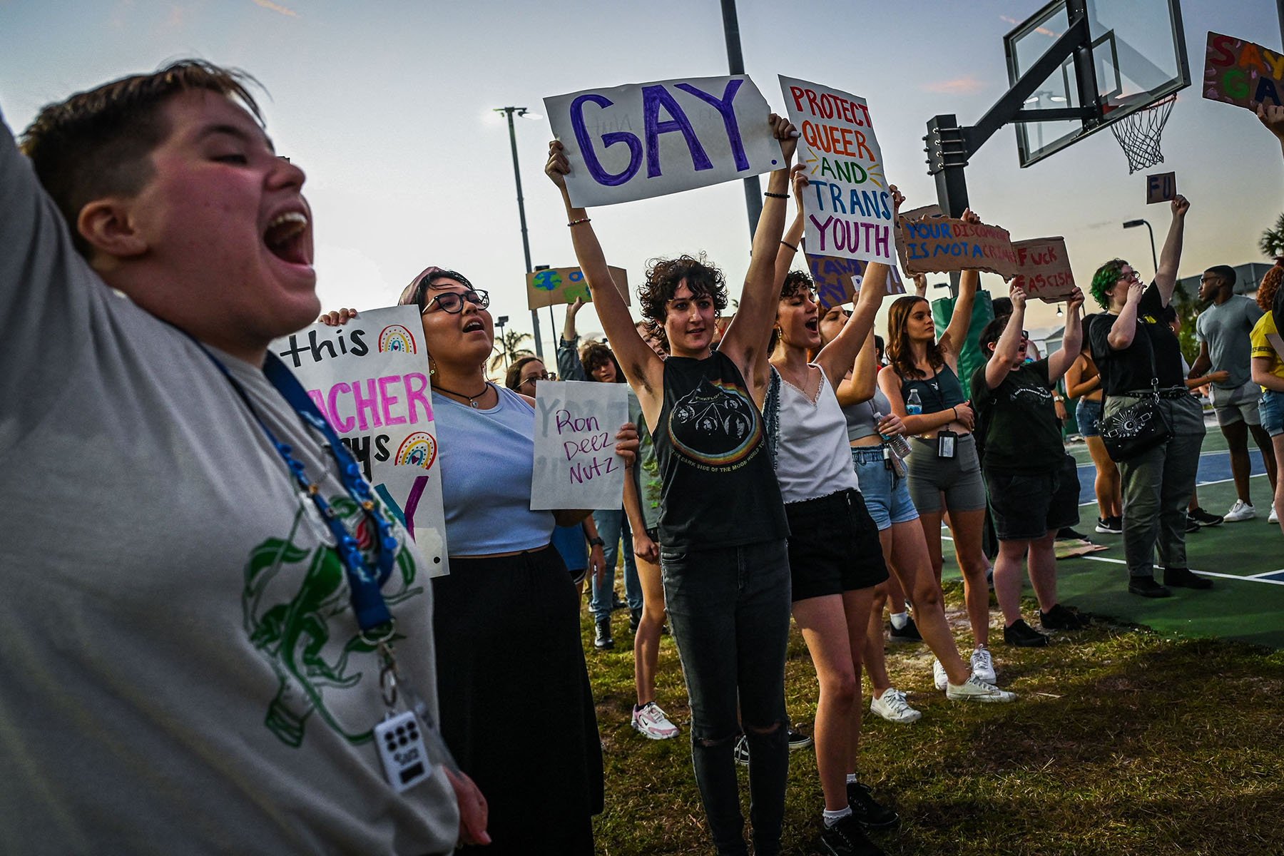 Young LGBTQ+ rights supporters hold signs and protest against Florida Governor Ron DeSantis outside a Trump campaign event.