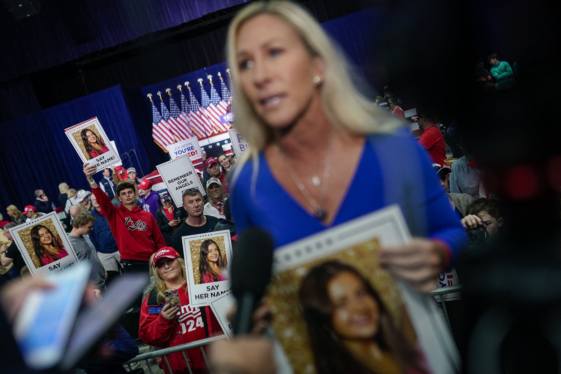 Rep. Marjorie Taylor Greene speaks to reporters as supporters of former President Donald Trump hold images of Laken Riley before he speaks at a campaign rally.
