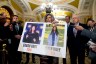 Sen. Joni Ernst holds a poster with photos of murder victims Sarah Root and Laken Riley as she is surrounded by press and other senators.