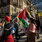A coalition of queer and transgender Muslim and Jewish people, as well as LGBTQ+ Arabic hold placards and Palestinian flags demonstrate during a protest.