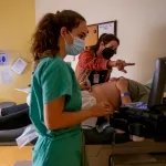 A family physician and her resident perform an ultrasound on a young woman in an examination room.