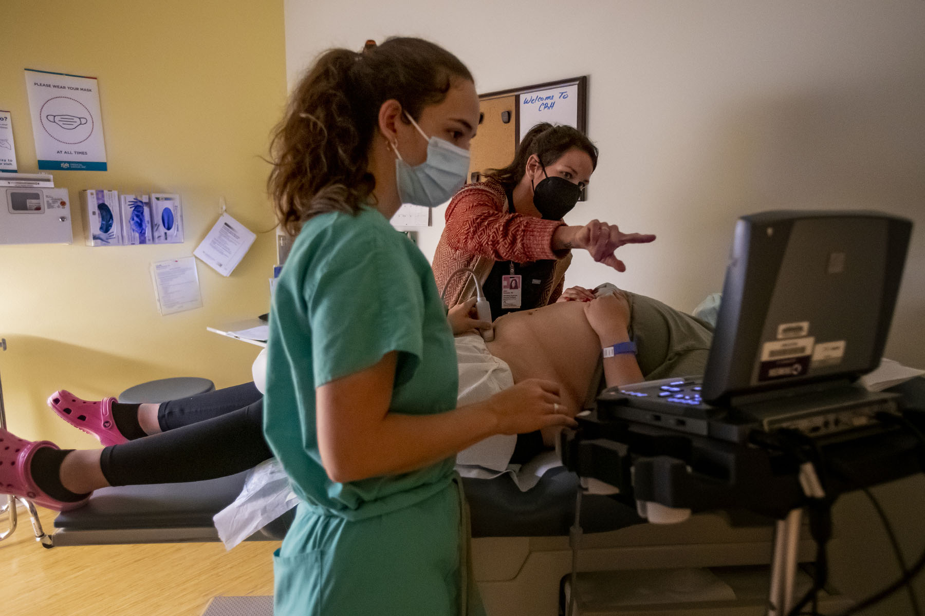 A family physician and her resident perform an ultrasound on a young woman in an examination room.