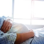 Close-up of a pregnant woman's belly in a hospital bed with a catheter in hand.