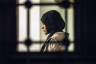 A woman is seen praying through a window at a mosque.