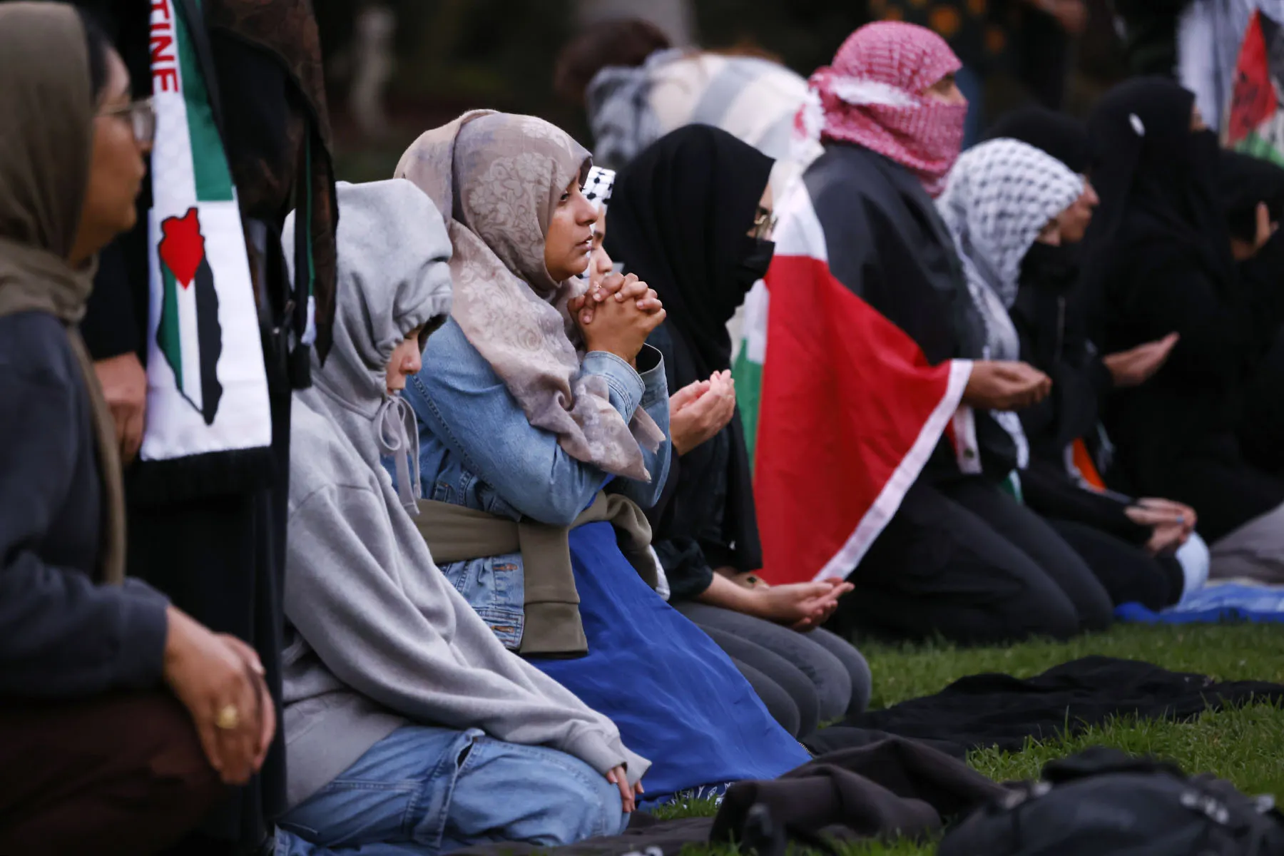 Protesters wearing hijabs and Palestinian flags pray at a park in Los Angeles during a protest.