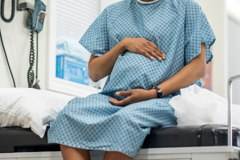 A young pregnant black woman sit up on an exam table in her doctors office during a routine prenatal check-up.