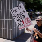 An advocate for cooling Texas prisons walks past a makeshift cell during a rally on the steps of the Texas Capitol. She is holding a sign that reads 