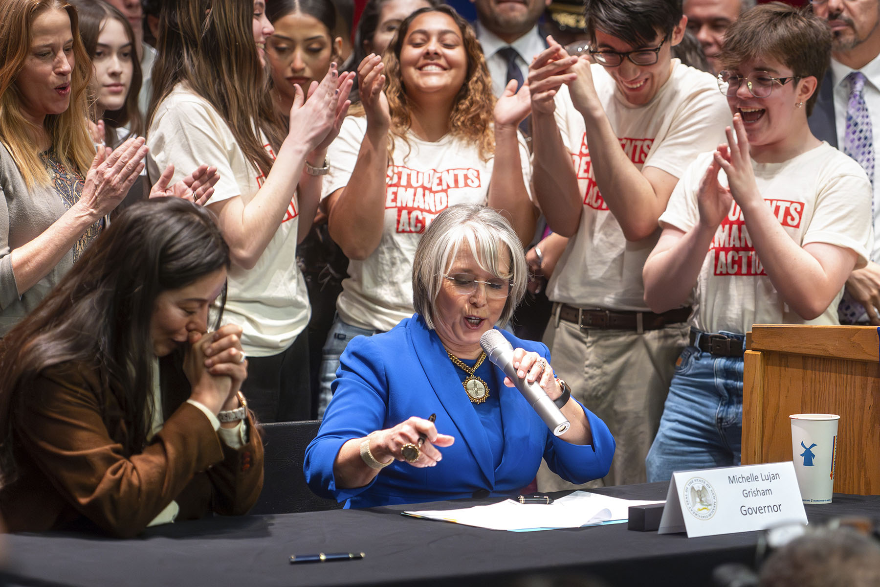 Gov. Michelle Lujan Grisham prepares to sign House Bill 129 at West Mesa High School as students clap and cheer around her.