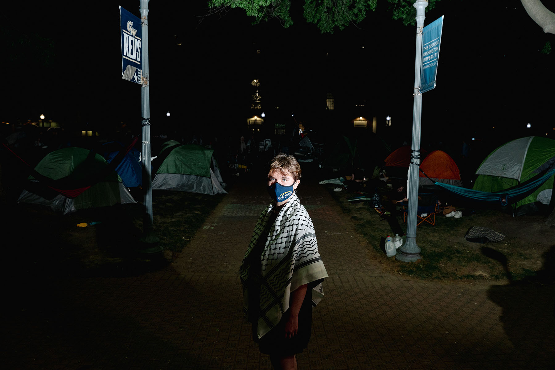 Elizabeth poses amidst tents at the George Washington University encampment. She is wearing a face mask and is drapped in a keffiyeh.