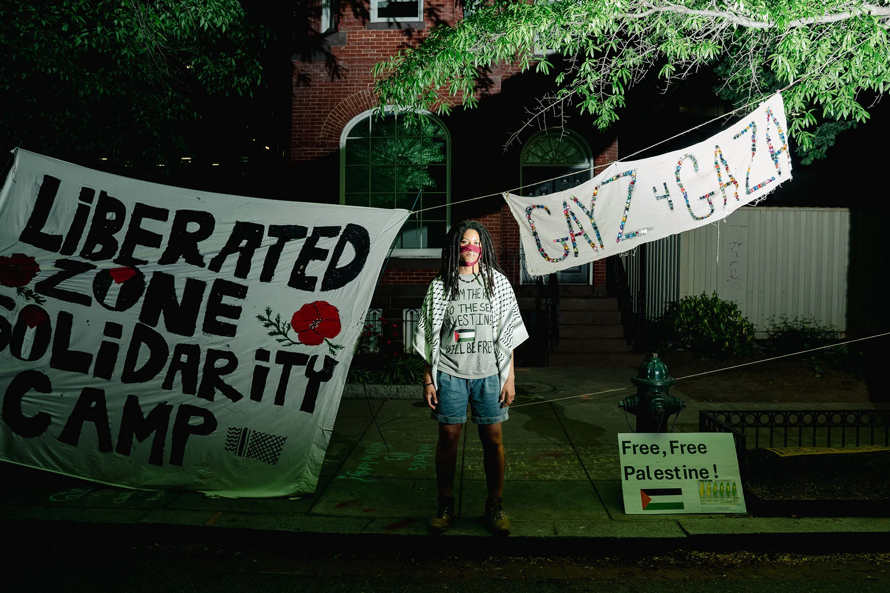 Bobbi-Angelica Morris poses for a portrait at University Yard on the George Washington University campus in front of signs that read "Liberated zone solidarity camp" and "GAYZ 4 GAZA"