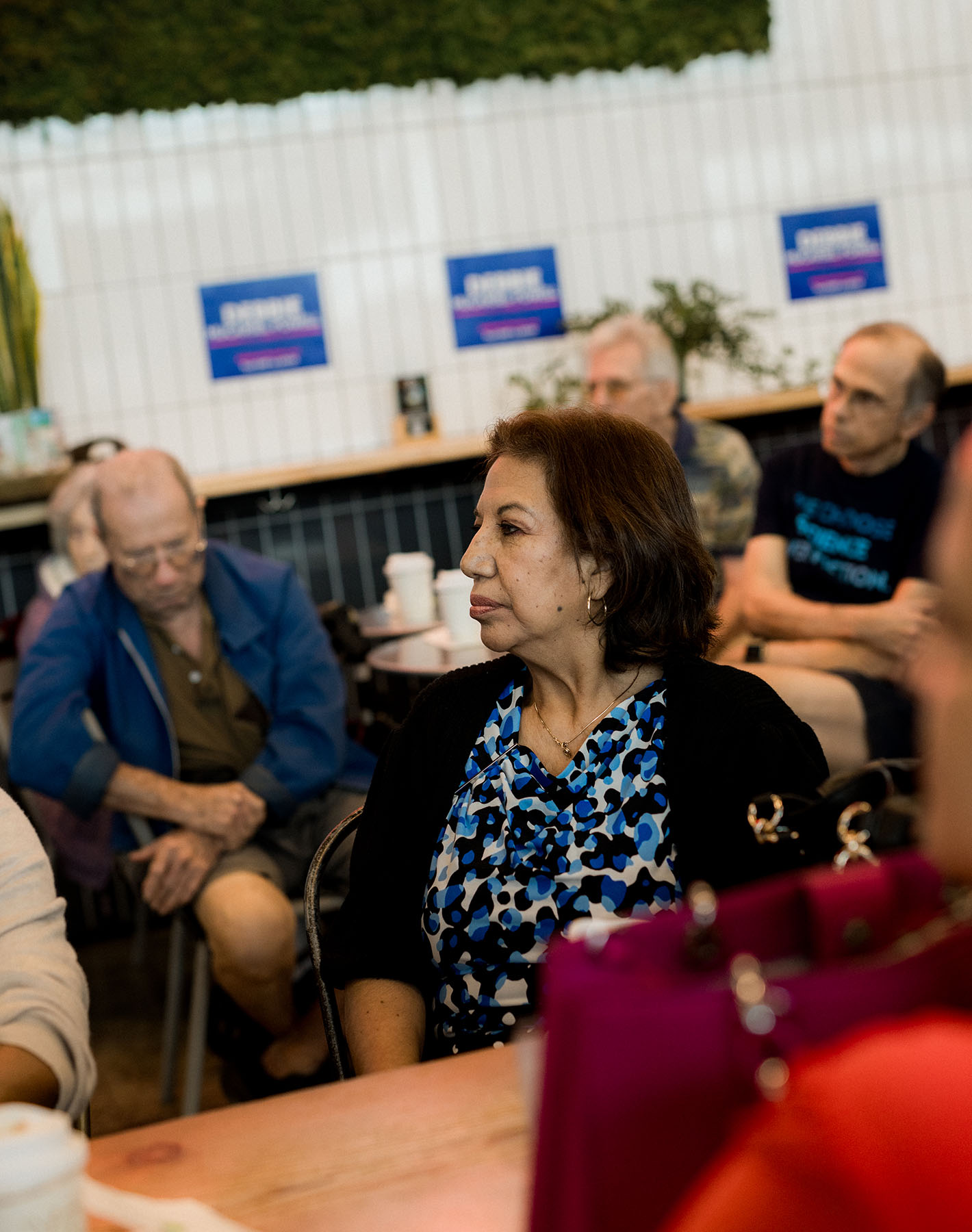 A woman listens as Debbie-Mucarsel-Powell speaks to a crowd in a coffee shop.