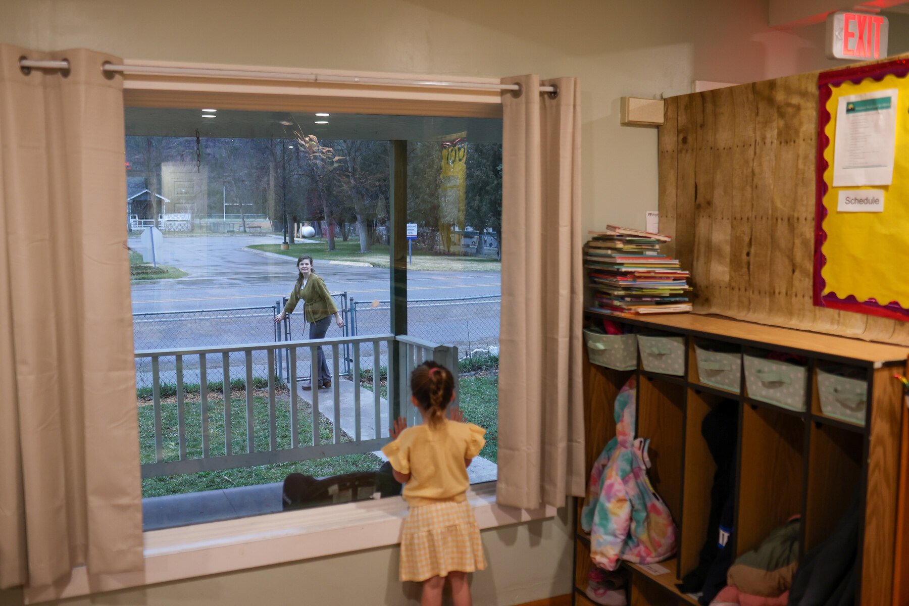 A preschool student watches her mom leave from a window after dropping her off at day care.