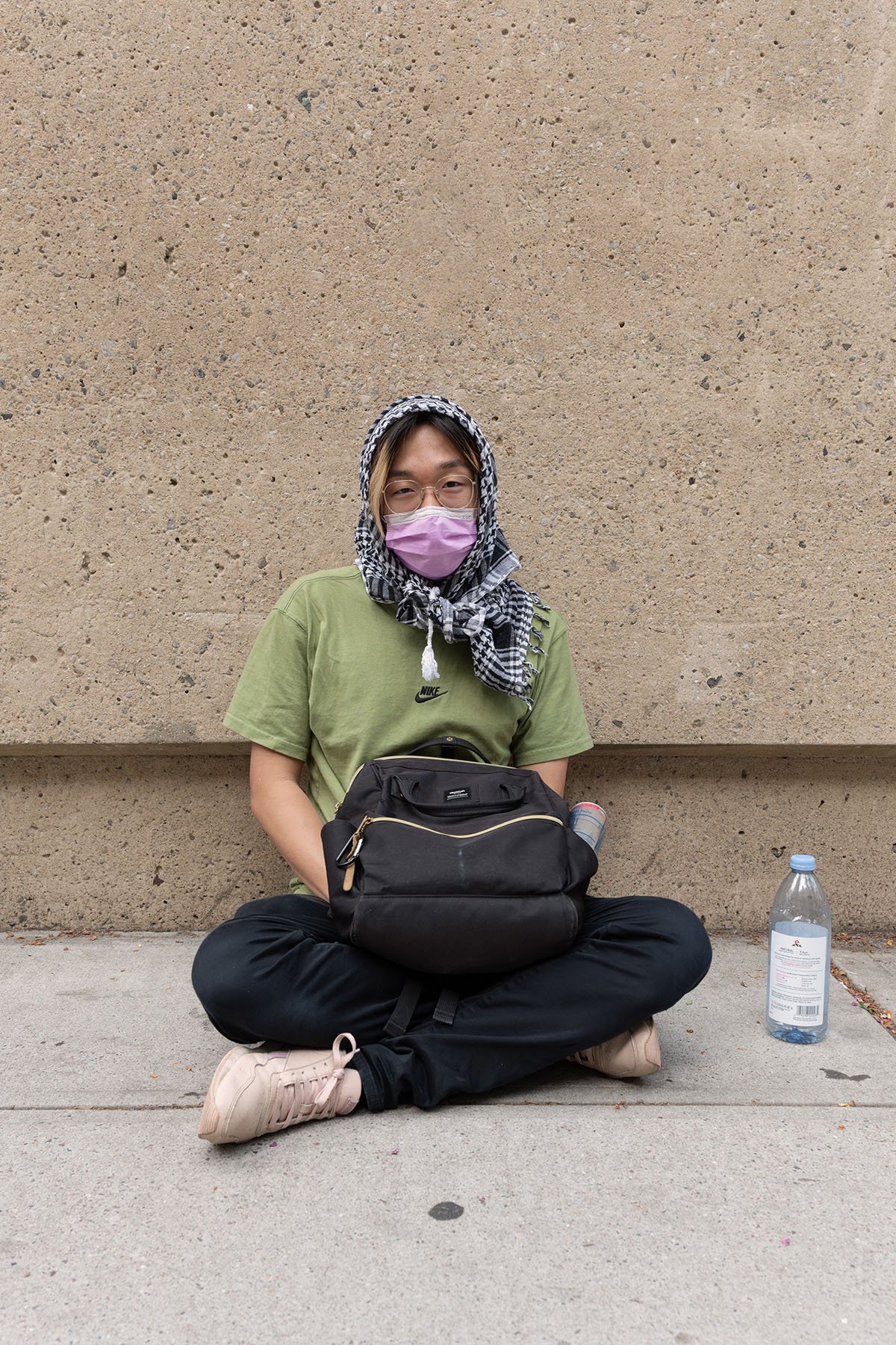 Warren, wearing a mask and a keffiyeh rests against the Lowenstein Building at the Lincoln Center Campus of Fordham University.