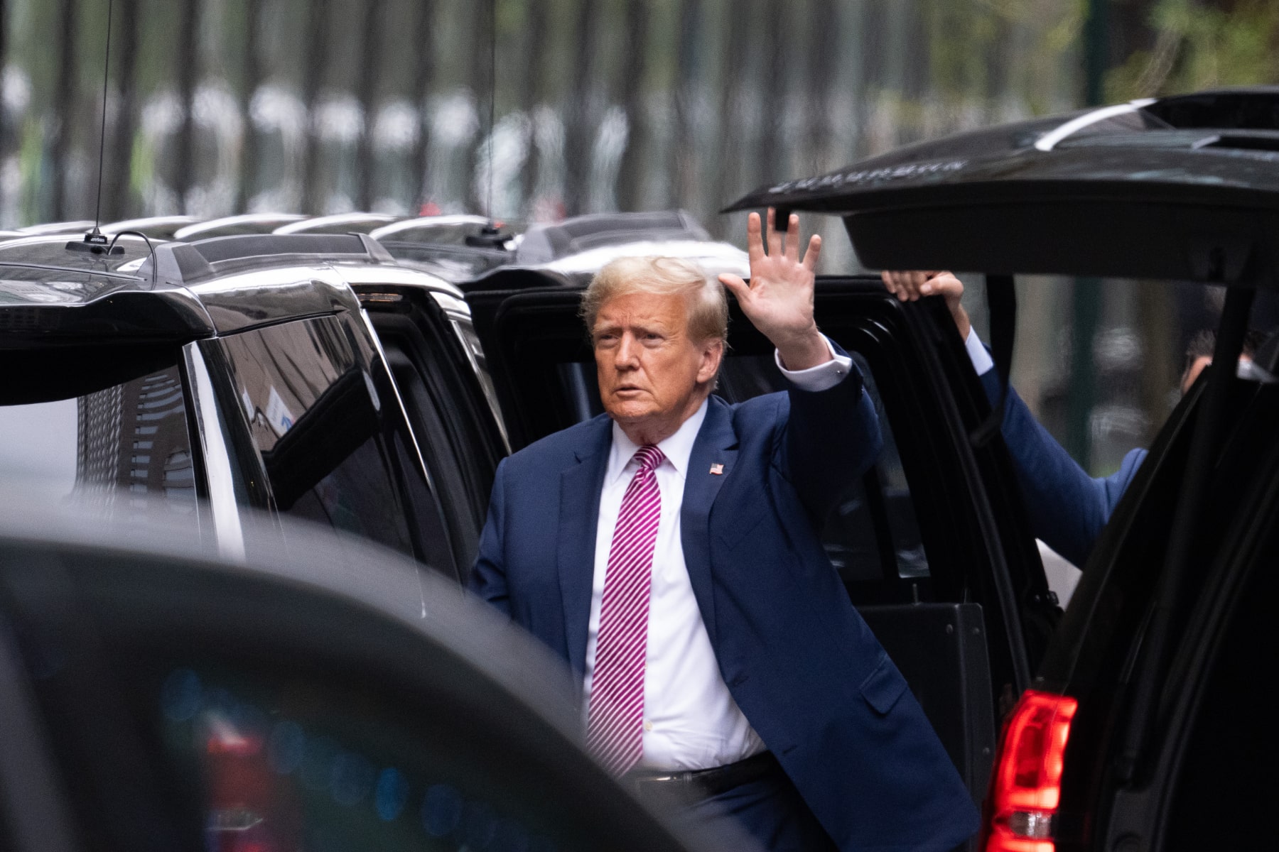 Donald Trump, standing near SUVs, waves outside Trump Tower