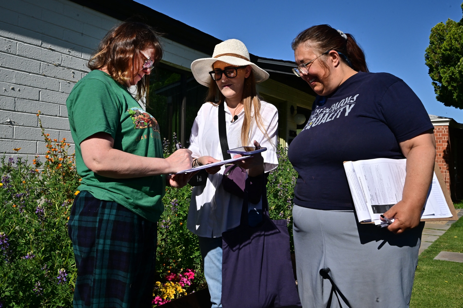 Lucy Meyer, left, signs a paper on a clipboard outside her house as canvassers Liz Grumbach, center, and and Patricia Jones, right, look on