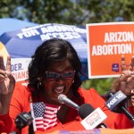 Chris Love of Arizona for Abortion Access speaks, flanked by people holding signs that say Arizona for Abortion Access