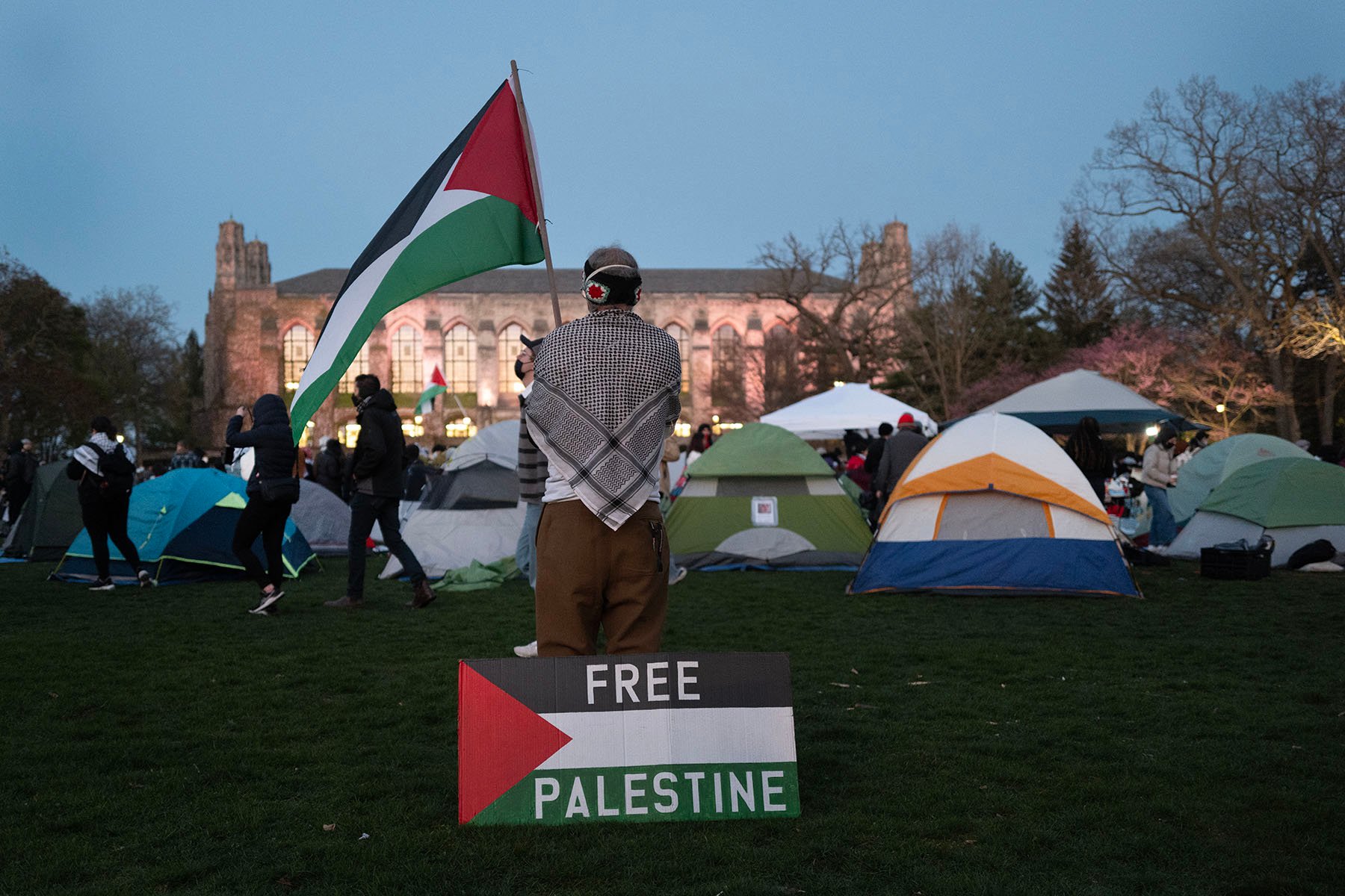 A man is seen wearing a keffiyeh and waving a Palestinian flag as people rally at the pro-Palestinian encampment on the campus of Northwestern University.