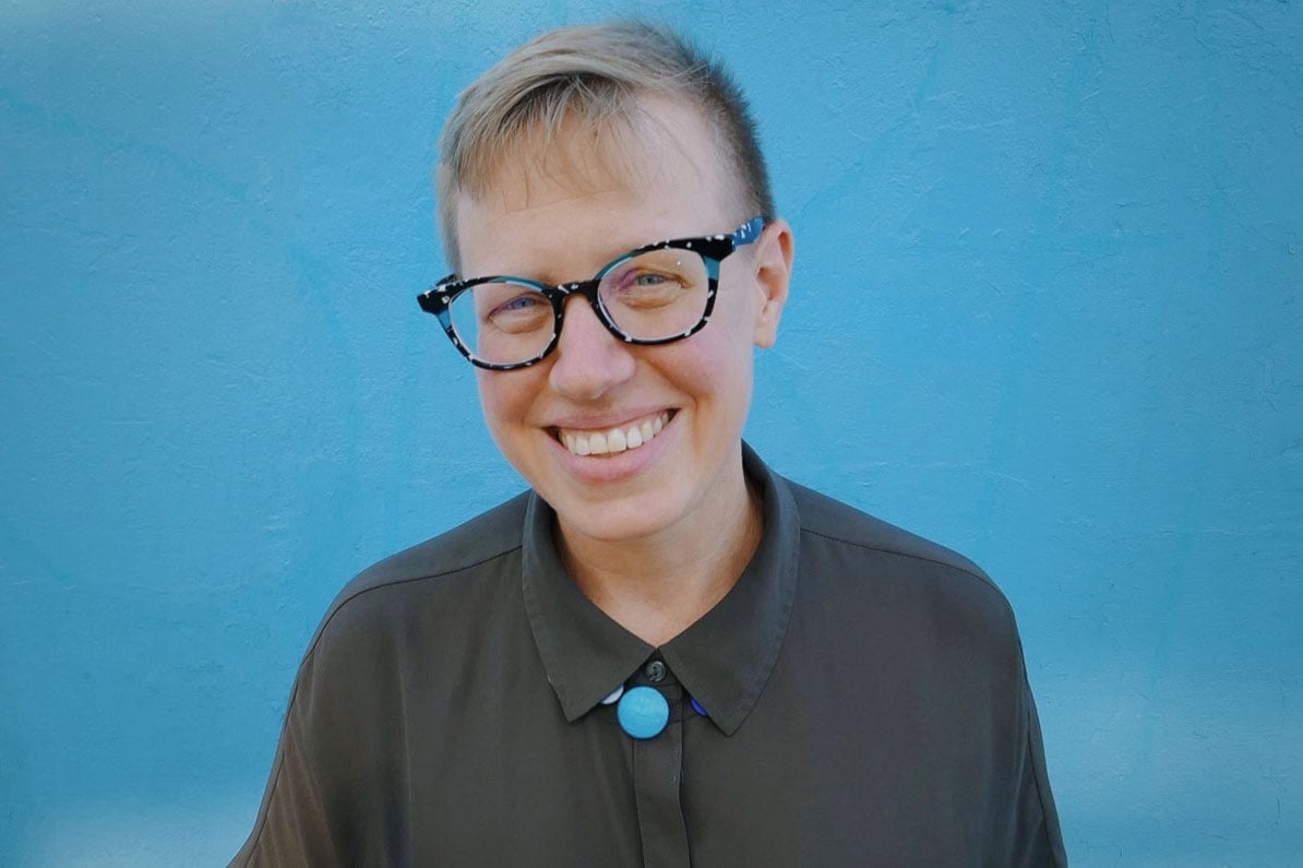 Portrait of Emily Drabinski smiling against a blue wall.