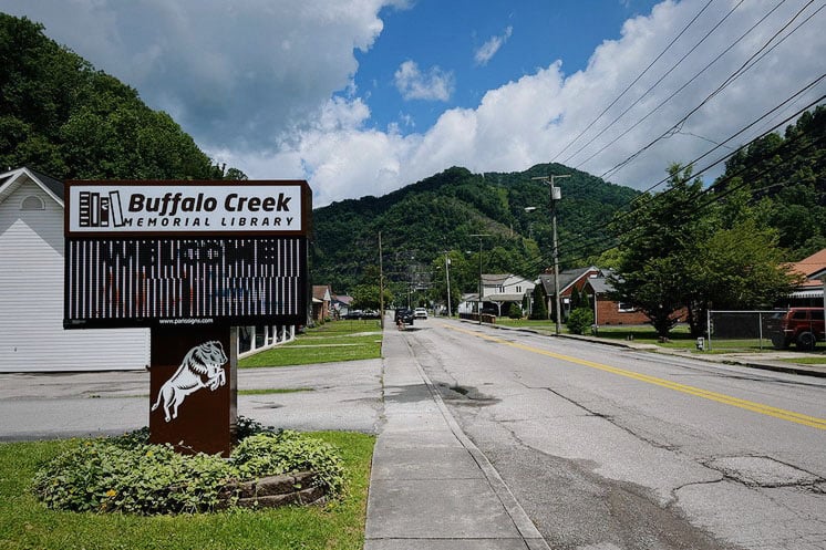 A sign for Buffalo Creek Memorial Library is seen along a road. In the background, rolling hills can be seen.