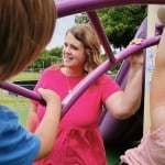 A Kindergarten teacher speaks with kids as they play on the monkey bars.