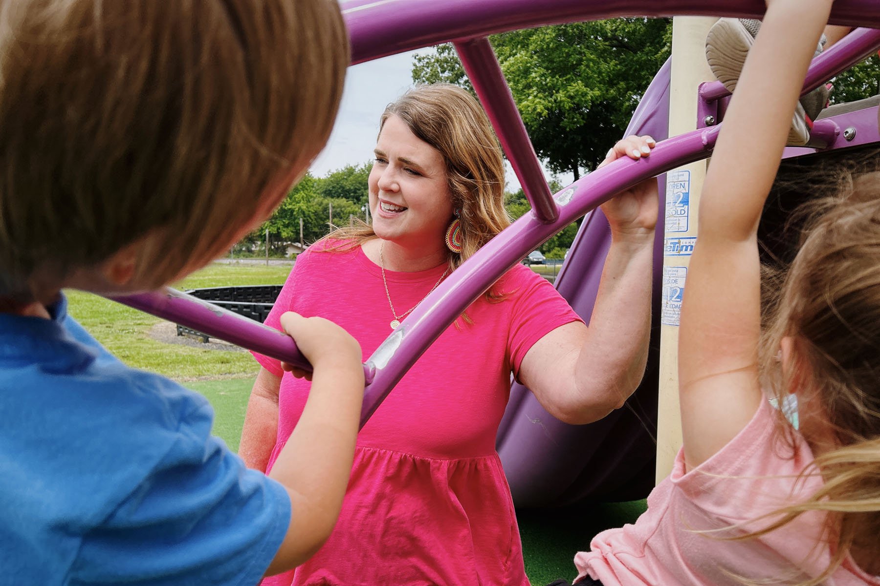 A Kindergarten teacher speaks with kids as they play on the monkey bars.