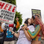 Two women kiss in reaction to confrontational Evangelical Christians condemning the annual LA Pride Parade. Behind them, a protester holds a large panel that reads 