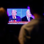 People are silhouetted in front of a tv screen showing Trump and Biden debating in a split screen