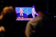 People are silhouetted in front of a tv screen showing Trump and Biden debating in a split screen