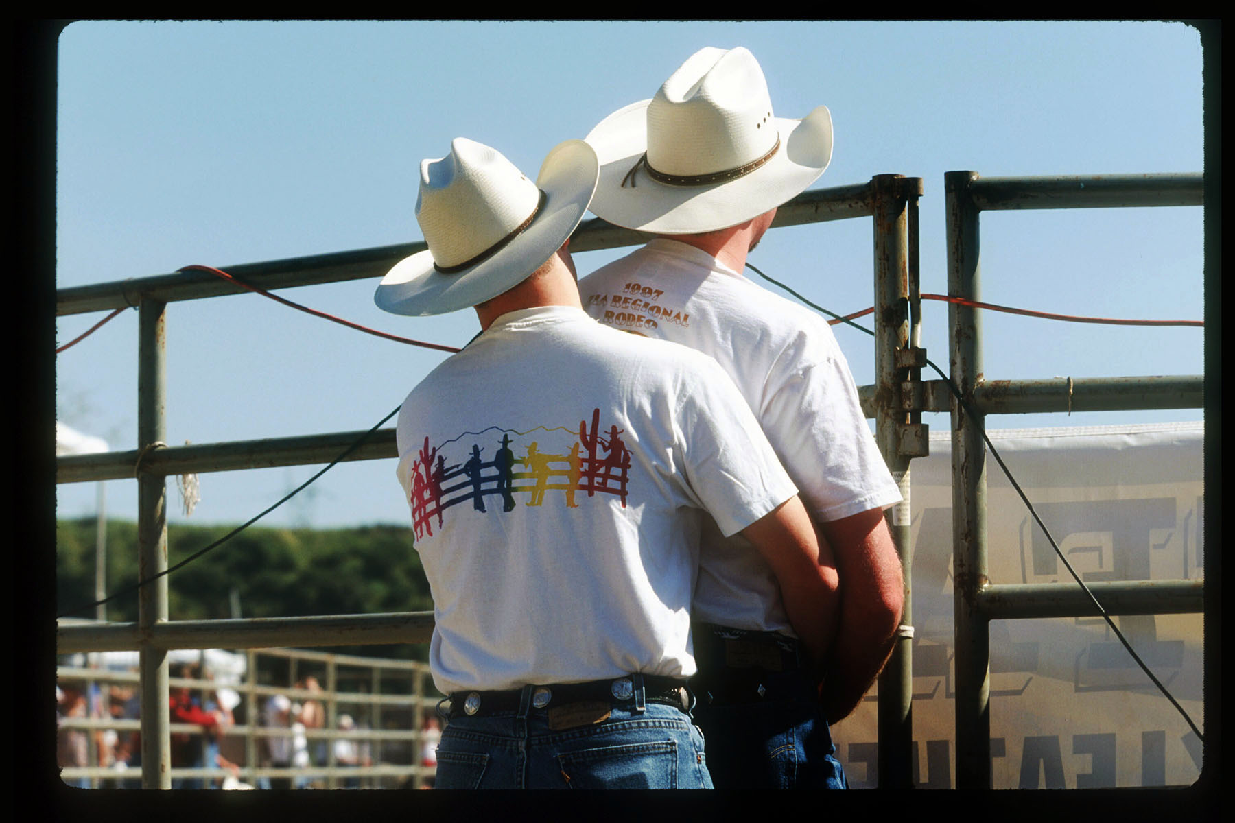 Two men hold each other in front of a gate at the Los Angeles Gay Rodeo.