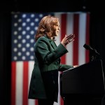 Vice President Kamala Harris delivers remarks at an event. An American flag is seen in the background.
