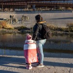 A mother and child look across the bank of the Rio Grande towards the U.S. Mexico border where Texas National Guard troops are posted.