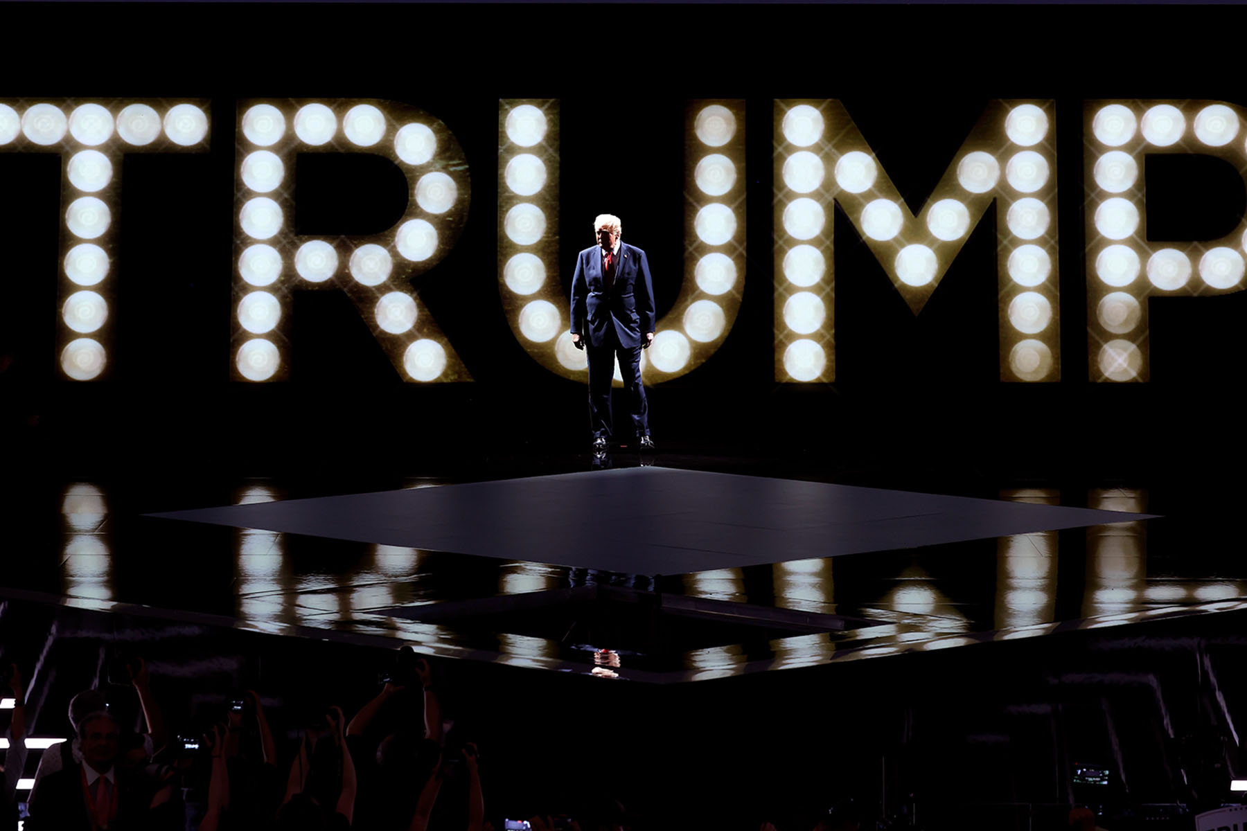 Former President Donald Trump arrives to speak on stage on the fourth day of the Republican National Convention. Behind him, spotlights spells out "Trump."