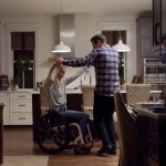 Mallory Weggemann and her husband, Jay Snyder, hold hands as they dance together in a warmly-lit kitchen at night.