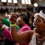 A black woman raises her fist as she cheers during a Biden-Harris campaign rally.