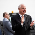 Minnesota Gov. Tim Walz smiles as he awaits the arrival of Vice President Kamala Harris at the Minneapolis-St. Paul International Airport.