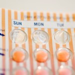 A close-up of a birth control pill pack. The package is striped in orange and white.