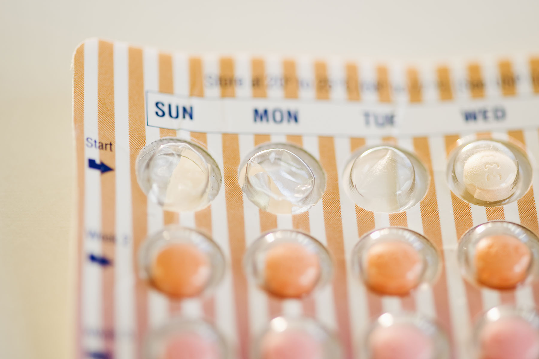 A close-up of a birth control pill pack. The package is striped in orange and white.