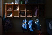 A set of cubbies and hooks are seen at a day care center. Each cubby contains various items like hats, scarves, and toys, while several backpacks hang from hooks below.