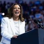 Vice President Kamala Harris, wearing a white suit and standing at a lectern and smiling, speaks in Savannah, Georgia