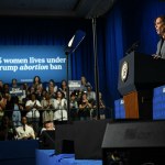 Vice President Kamala Harris stands at a lectern near a crowd sitting under a sign that says 