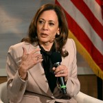 Vice President Kamala Harris sitting in front of a backdrop and an American flag holding a microphone