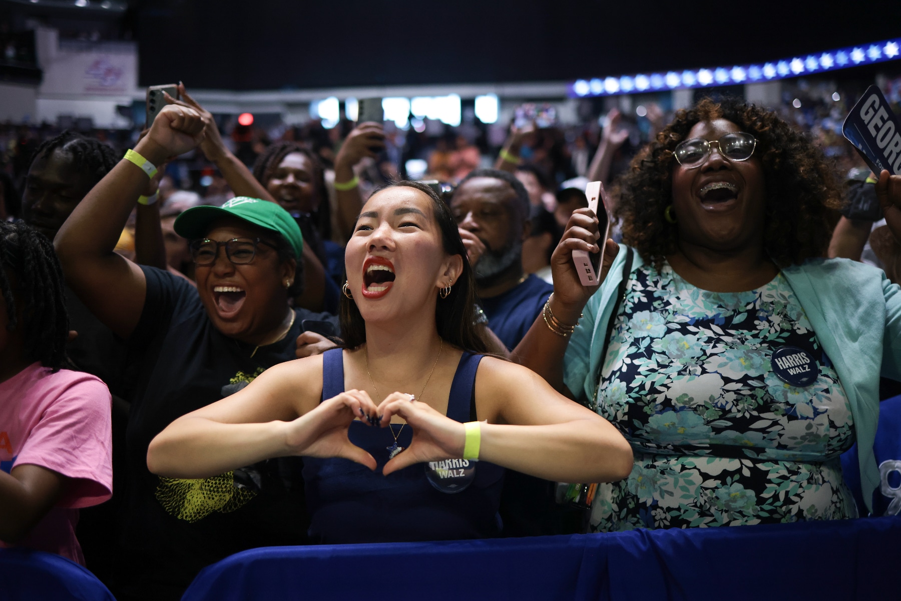 La gente anima a Kamala Harris en un evento de campaña, y una persona hace un corazón con sus manos mientras anima.