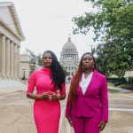 Cassandra Welchlin and Velvet Scott standing side by side in front of the Mississippi Capitol building. Cassandra, on the left, is wearing a bright pink dress, and Velvet, on the right, is dressed in a pink suit.